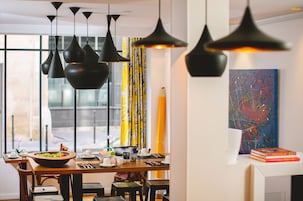 Un'area pranzo moderna con illuminazione a sospensione, un'ampia finestra con vista e un quadro astratto dai colori vivaci appeso al muro.