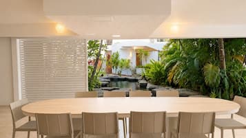 A dining area with a round table and chairs, a view of a garden with a water feature, and a white wall with horizontal slats.