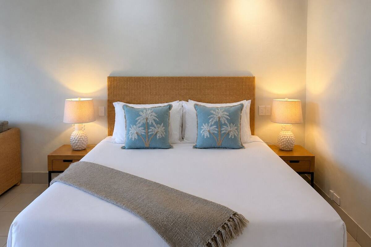 A neatly made bed with a woven headboard, two bedside lamps, and two matching pillows.
