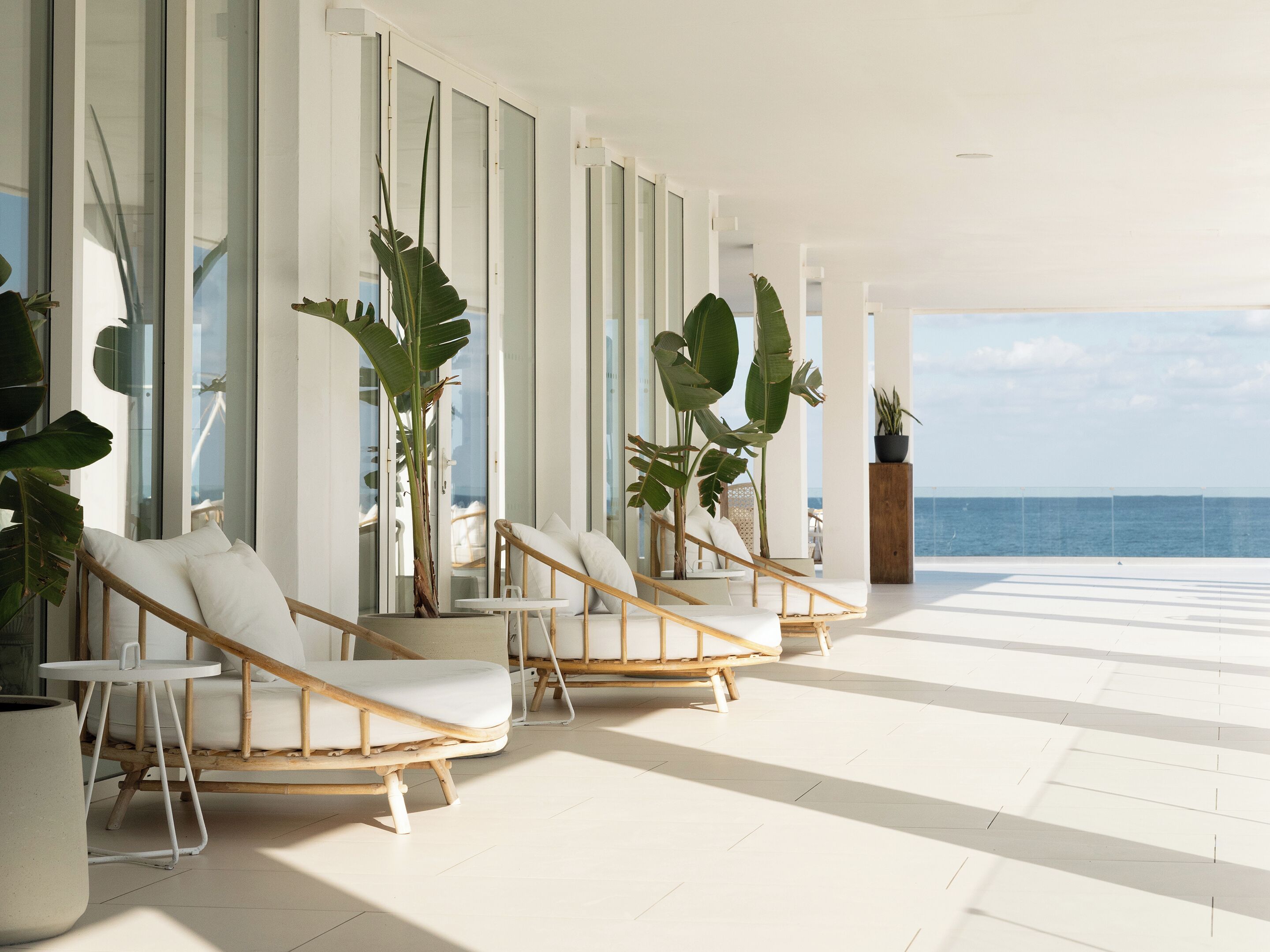 Un espace de vie moderne, à aire ouverte, doté de grandes fenêtres, de meubles blancs et de plantes tropicales.