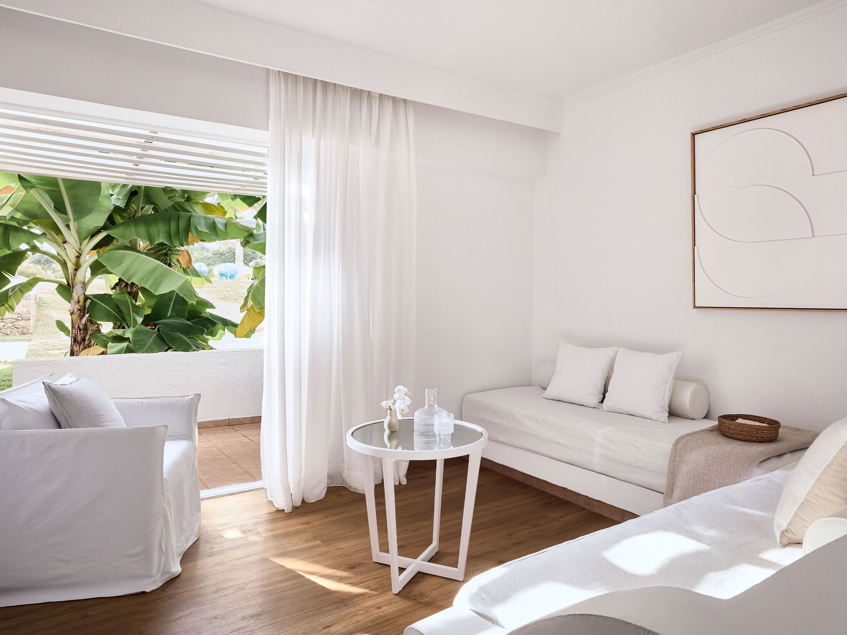 A modern, minimalist room with a white sofa, a round table, and a large window with sheer curtains.