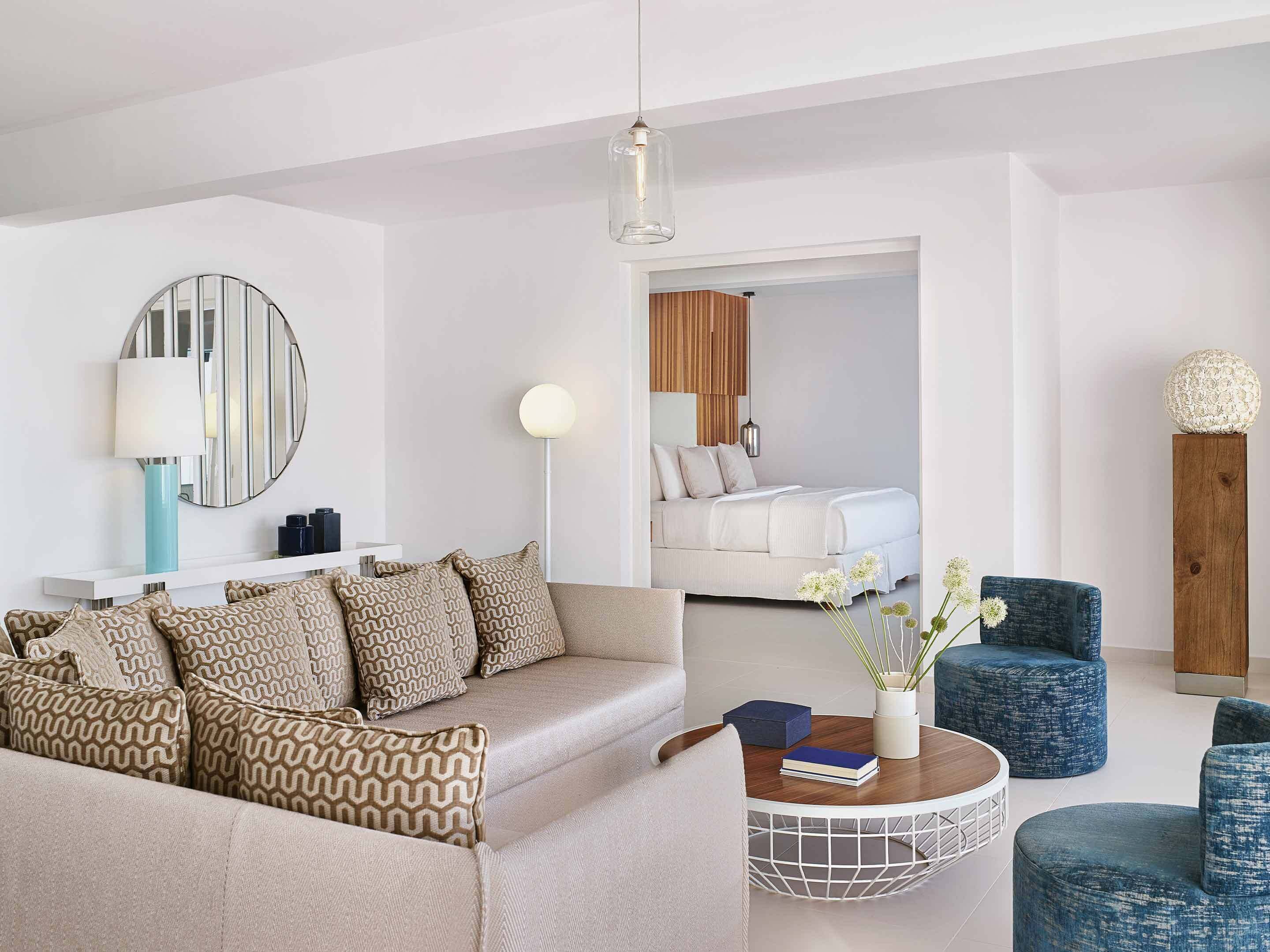 Una habitación de hotel moderna con sofá, una mesita de centro redonda y una cama con cabecera de madera.