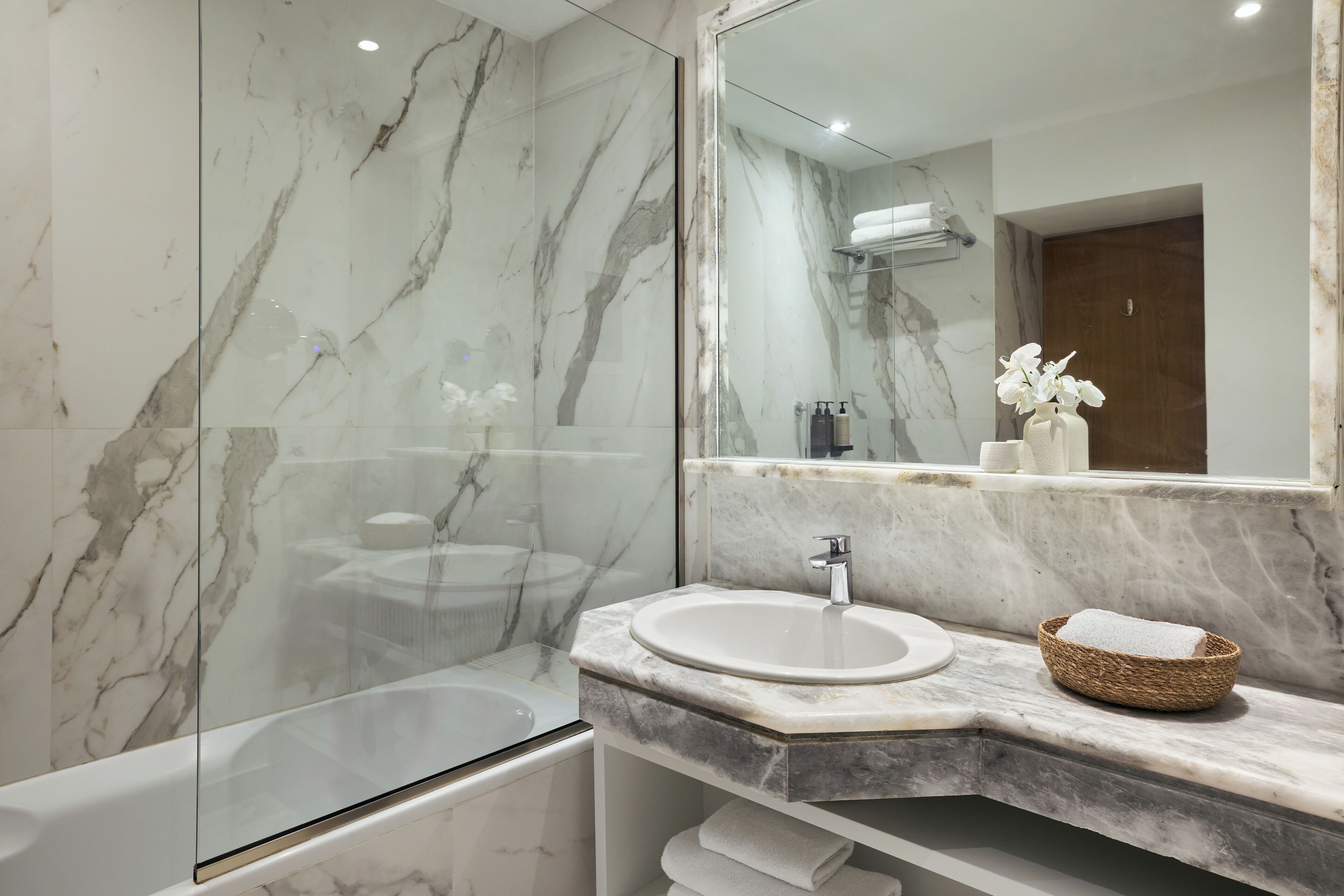 A modern bathroom with a marble vanity, a glass shower enclosure, and a large mirror reflecting the room.