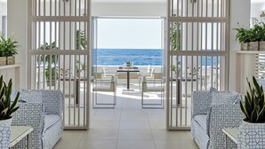 Un intérieur moderne avec vue sur la mer, comprenant un coin repas avec des meubles blancs et des plantes en pot.