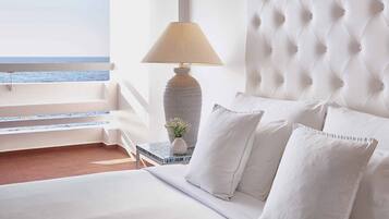 Ein Hotelzimmer mit Bett, Lampe, Blumen in einer Vase und Meerblick.