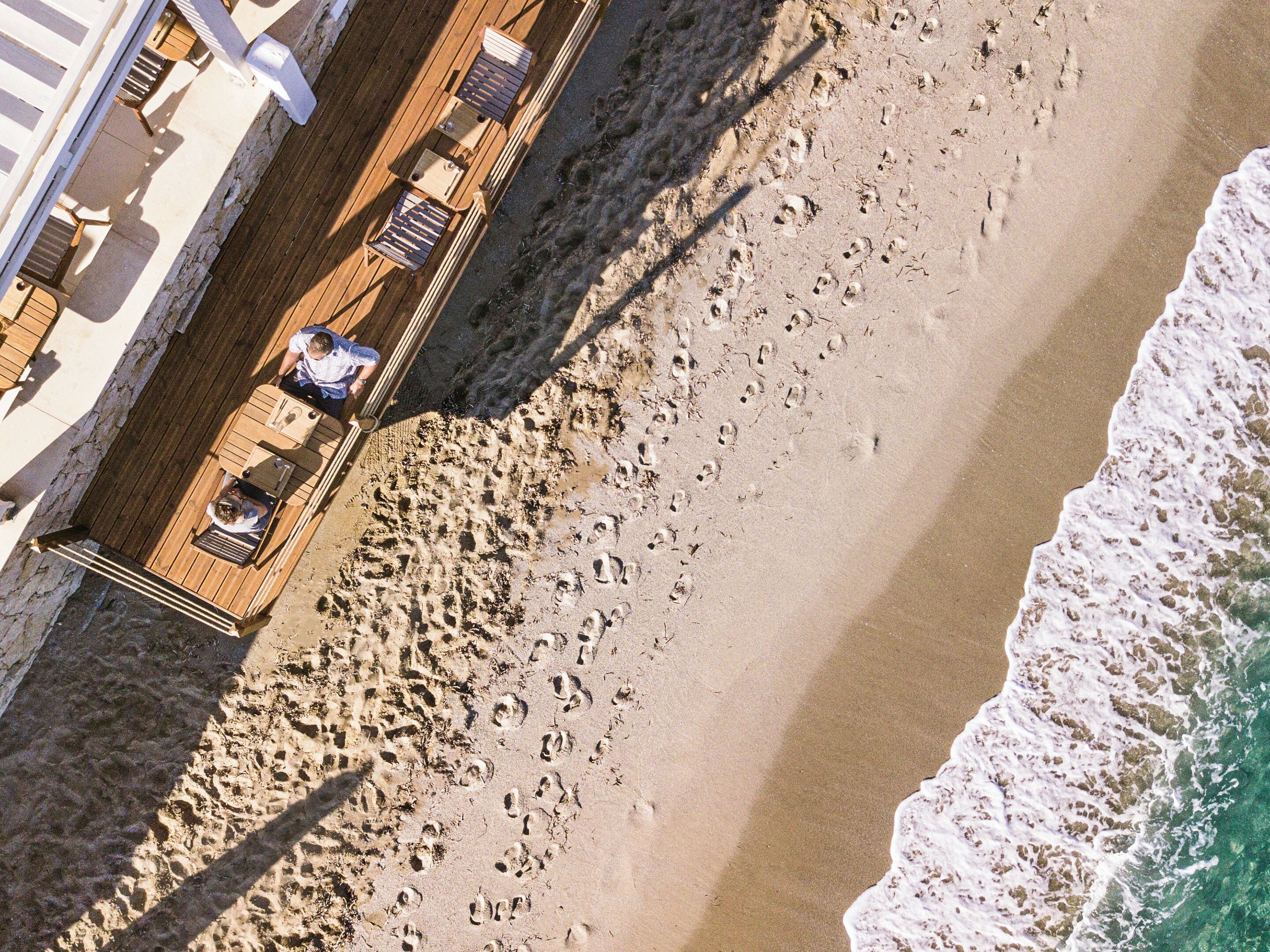 An aerial view of a beachside property with a wooden deck and outdoor seating.