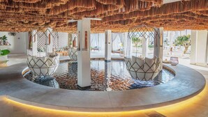 Un espace piscine intérieur luxueux, agrémenté de fauteuils suspendus et d’une fontaine centrale.