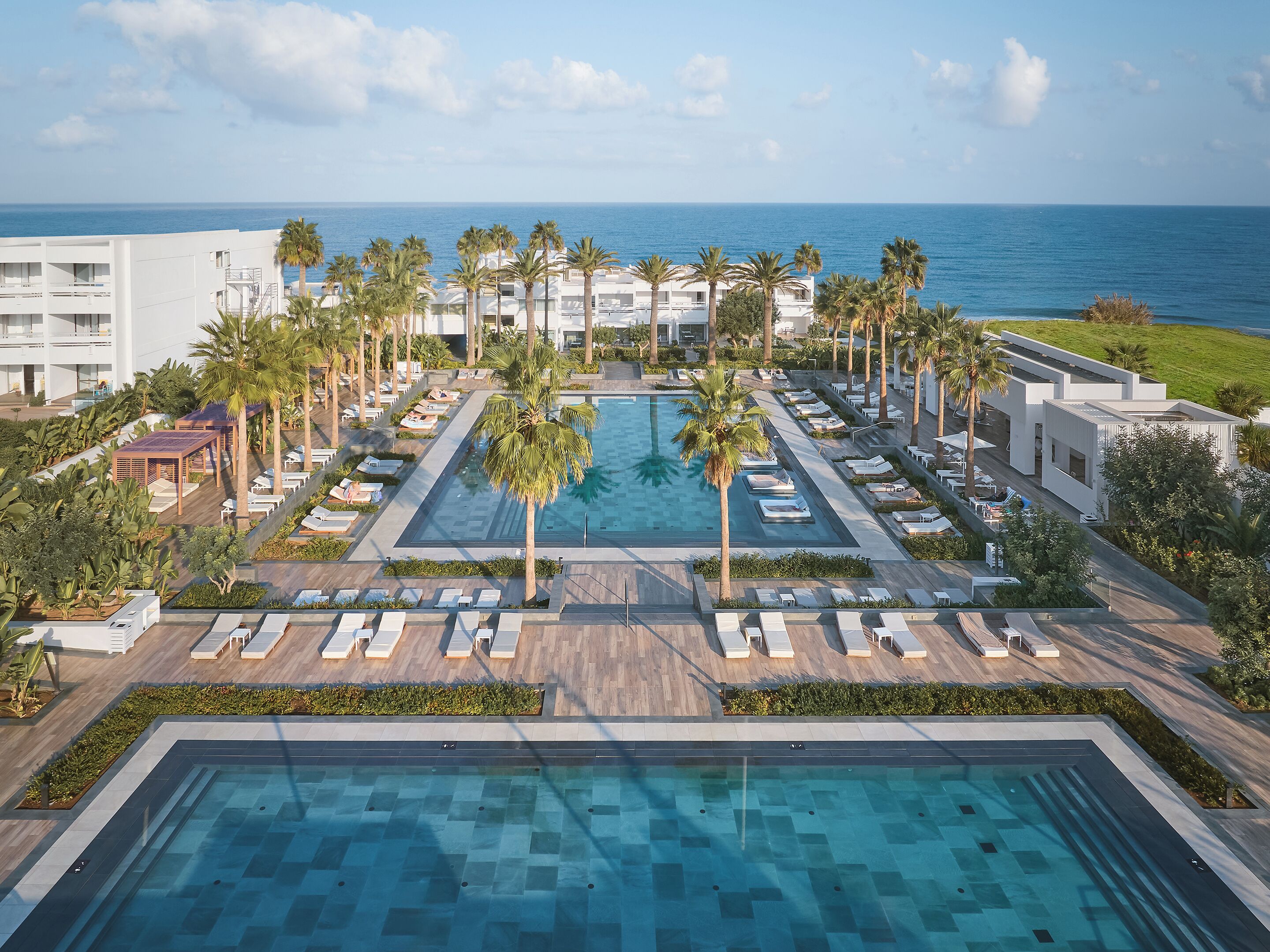 Een resort met een centraal gelegen zwembad, palmbomen en uitzicht op de oceaan.