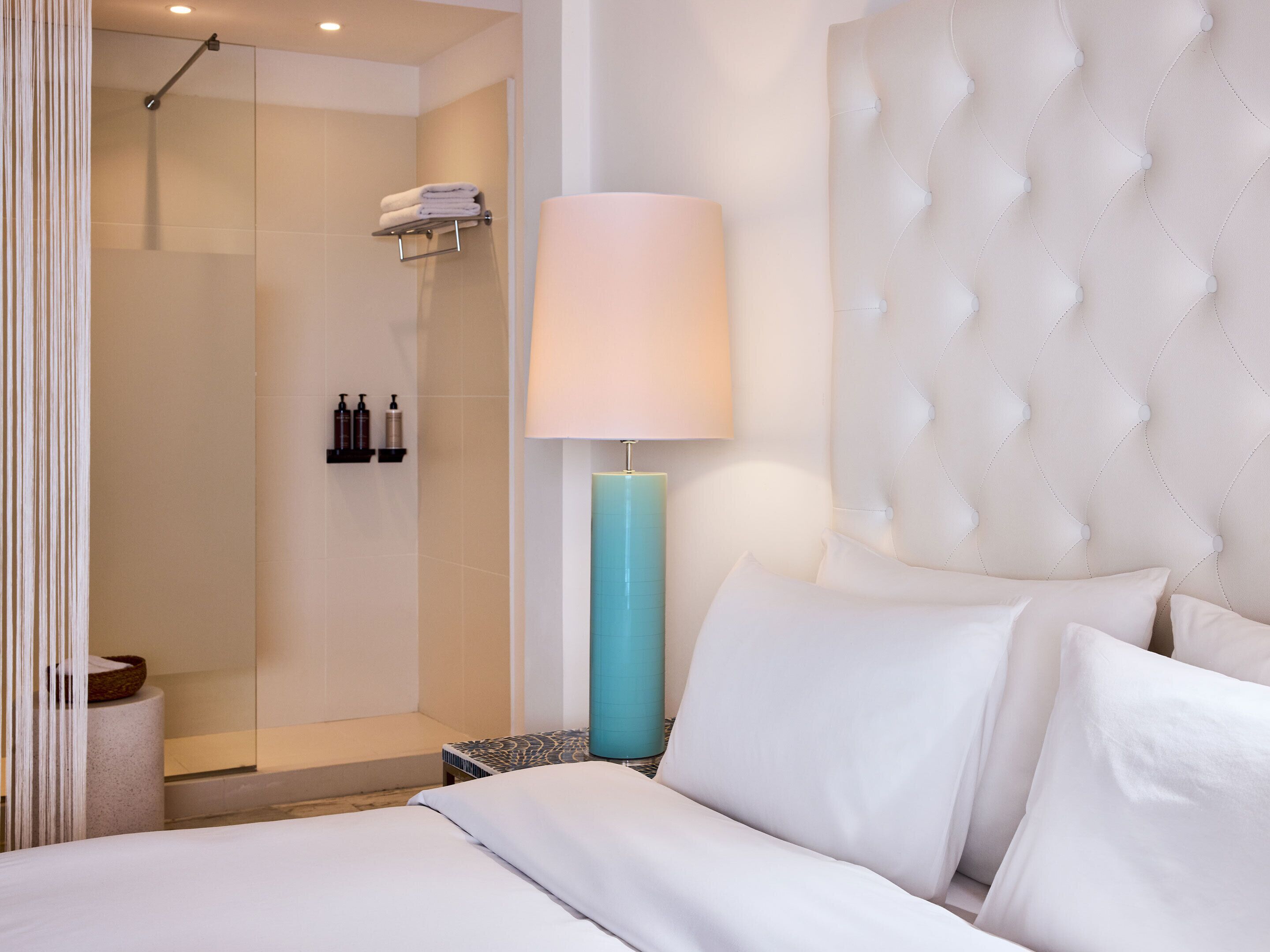 Une chambre d’hôtel moderne équipée d’un lit, d’une lampe de chevet, d’un espace douche et d’un porte-serviettes fixé au mur.