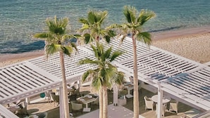 Un espace de détente aménagé sur la plage, avec des chaises longues blanches et des palmiers, offrant une vue sur la mer.