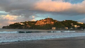A coastal landscape with a prominent hill featuring a lighthouse, surrounded by greenery and buildings. - Bahia del Sol Villas & Condominiums (San Juan del Sur)