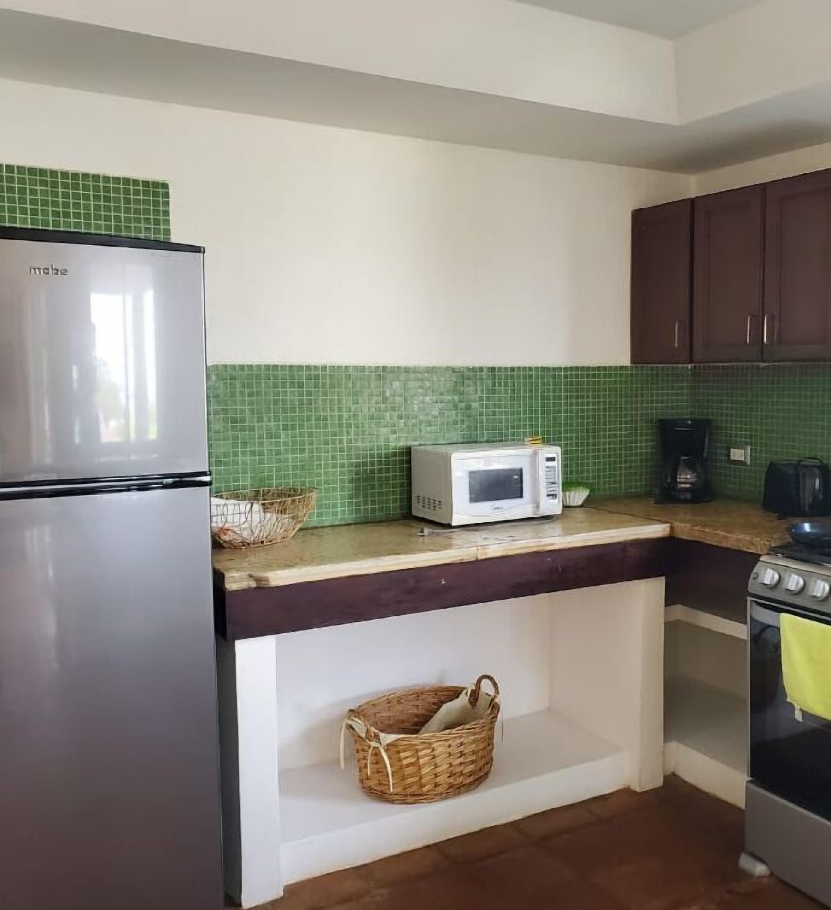 Cocina con refrigerador, microondas, estufa y salpicadero de azulejos verdes.