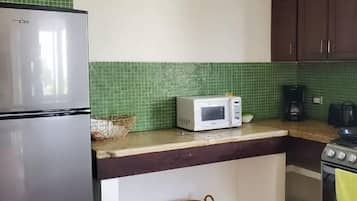 Cocina con refrigerador, microondas, estufa y salpicadero de azulejos verdes.