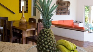A kitchen with a dining table, chairs, a fruit bowl with a pineapple and bananas, a vase, and a bright yellow wall. - Bahia del Sol Villas & Condominiums (San Juan del Sur)