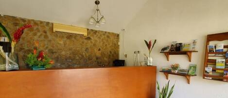 A reception area with a stone wall, wooden reception desk, potted plants, and a chandelier.