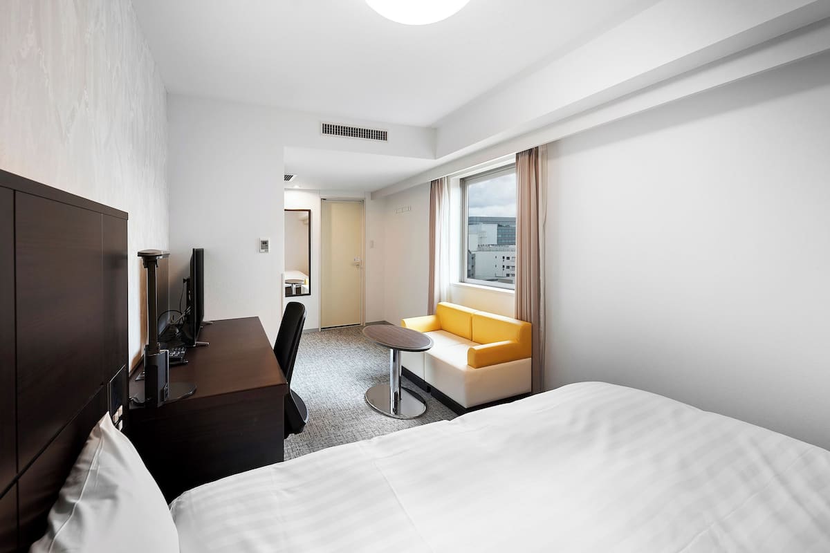 A hotel room with a bed, a desk with a computer, a sofa, and a window with curtains.
