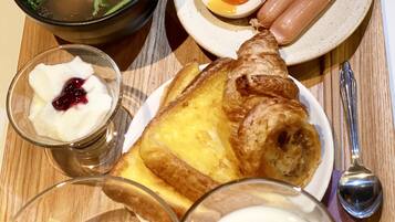 A breakfast tray with soup, eggs, sausages, toast, yogurt, and fruit.
