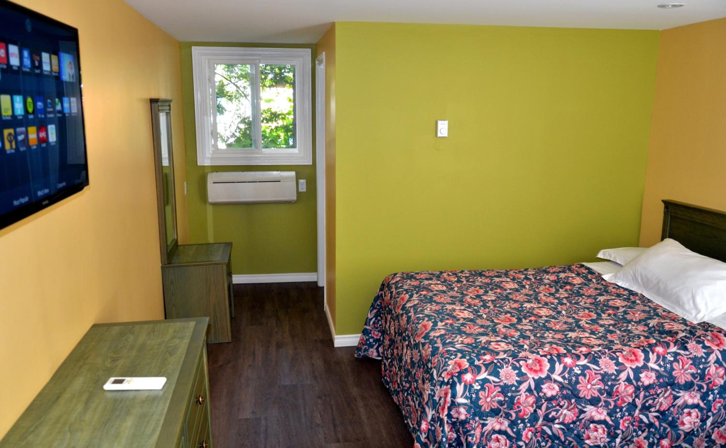 Una camera da letto con un letto, un comodino, una scrivania, una finestra e un condizionatore d'aria.