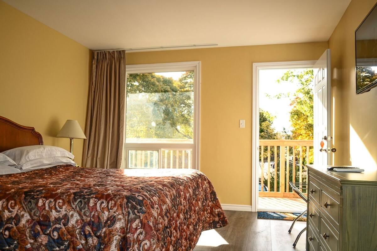 A bedroom with a bed, a dresser, a lamp, and a balcony with a railing.