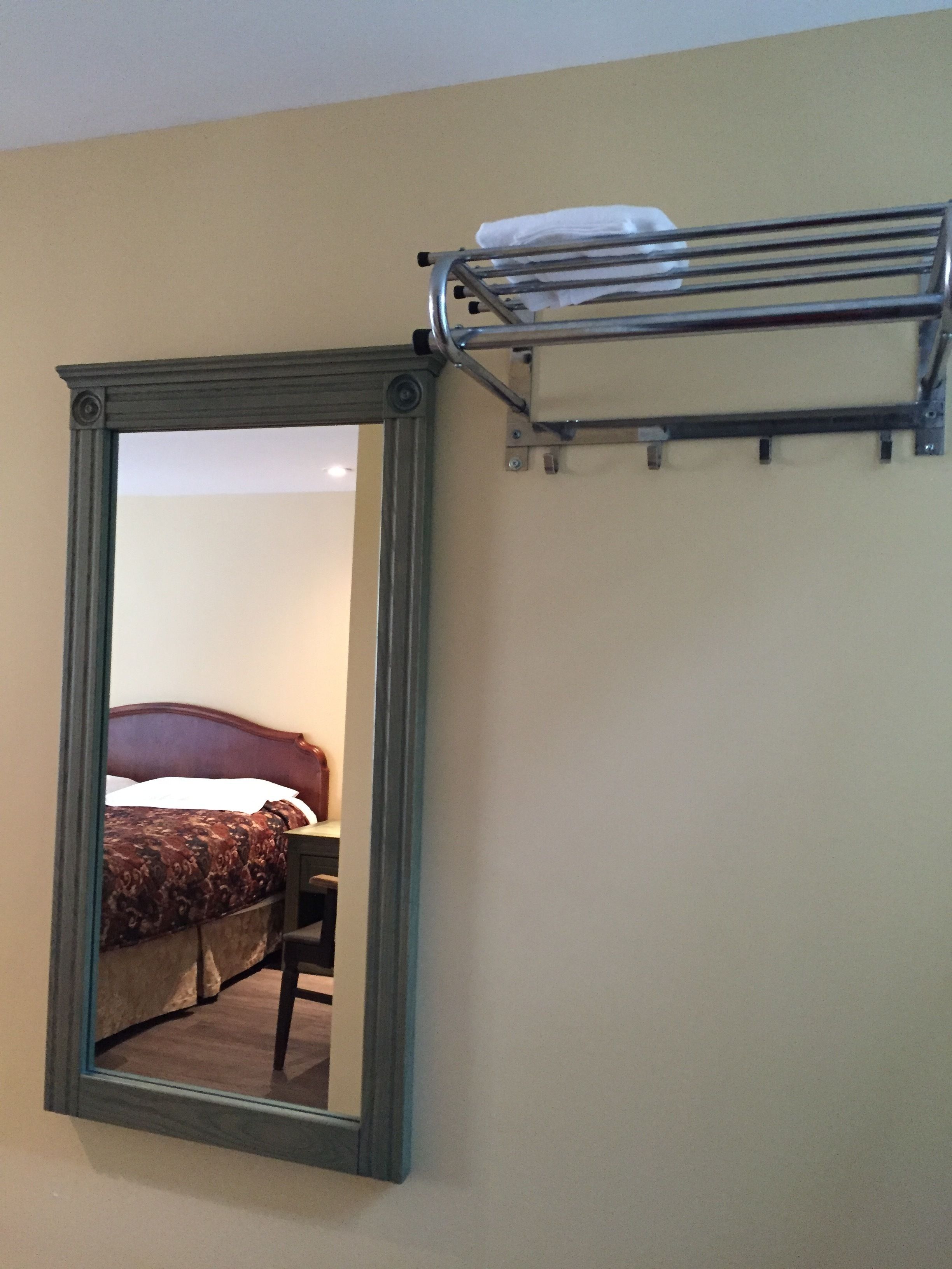 A room with a large mirror, a bed with a patterned bedspread, and a metal shelf above the mirror.
