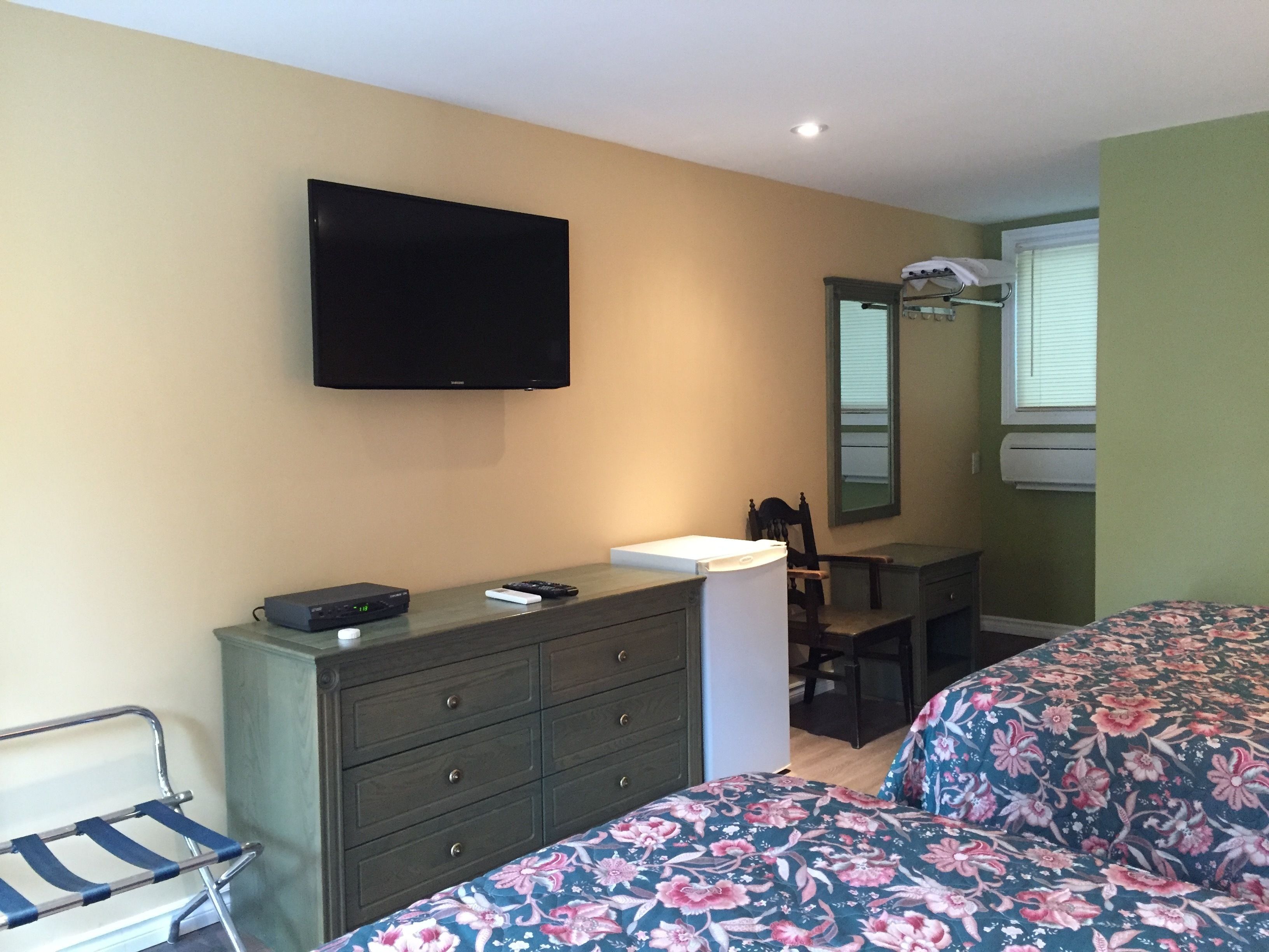 A bedroom with a bed, a dresser, a television, and a desk.