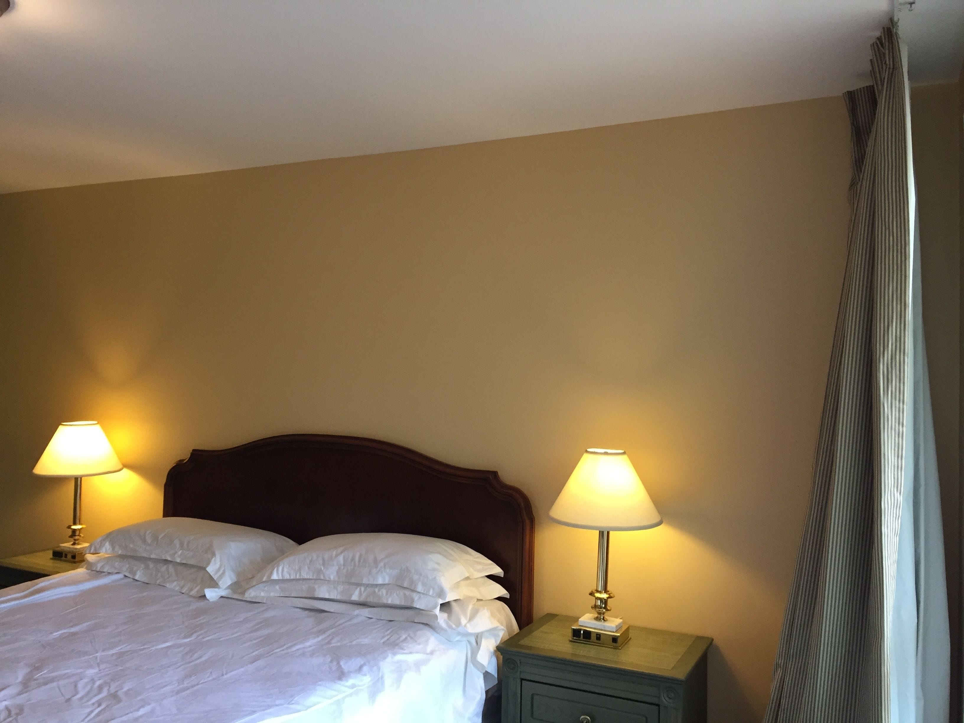 A hotel room with a bed, two bedside lamps, a nightstand, and a window with curtains.