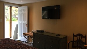 Un dormitorio con cama, cómoda, televisor montado en la pared y puerta que da a un balcón.