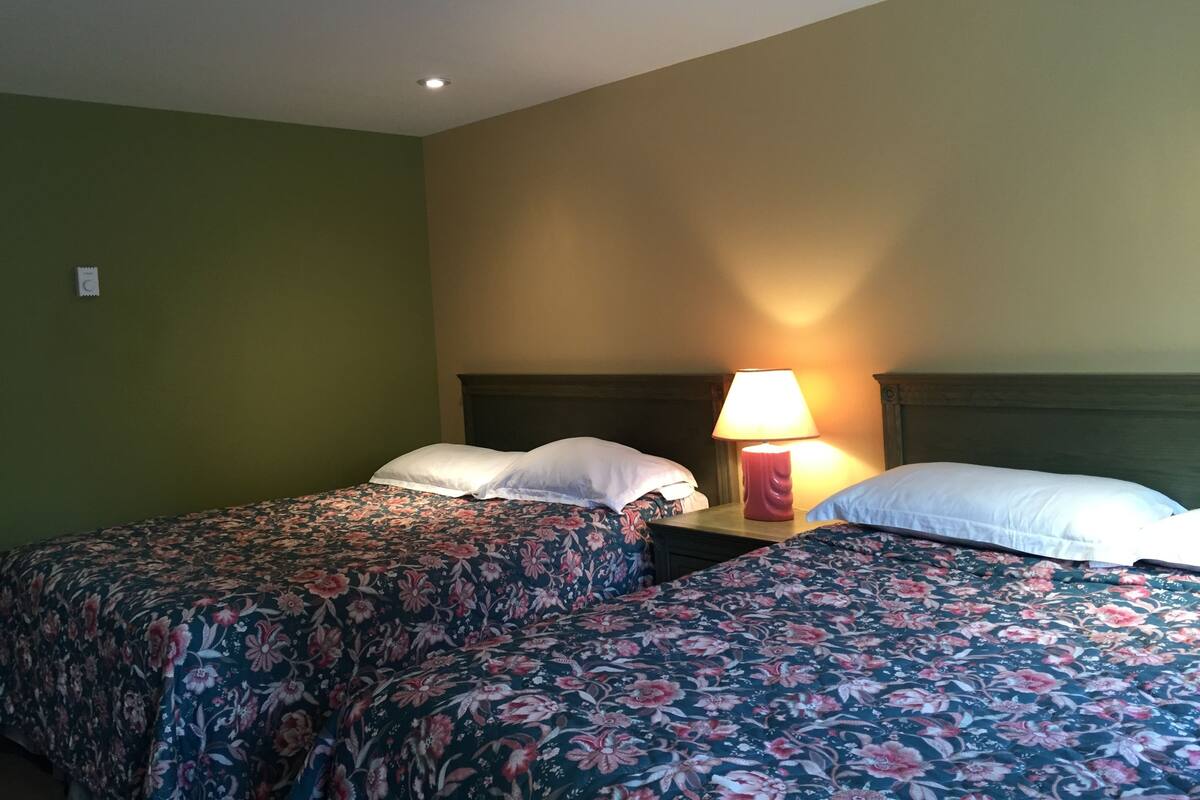 A hotel room with two beds, each with floral bedding, a nightstand with a lamp, and a green wall.