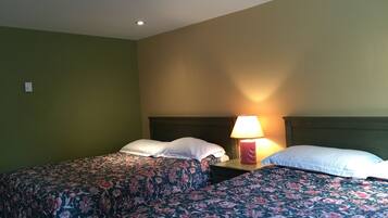 A hotel room with two beds, each with floral bedding, a nightstand with a lamp, and a green wall.