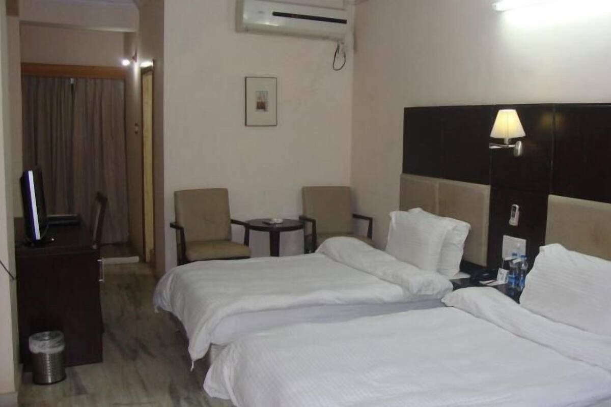 A hotel room with two beds, a desk, a chair, a lamp, and a trash can.