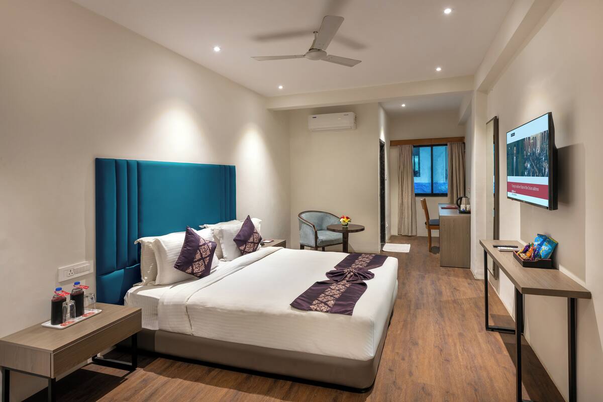 A modern hotel room with a large bed, a desk, a chair, and a TV.