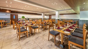 Un comedor amplio con mesas y sillas de madera, un diseño moderno de techo y un área de cocina visible al fondo.