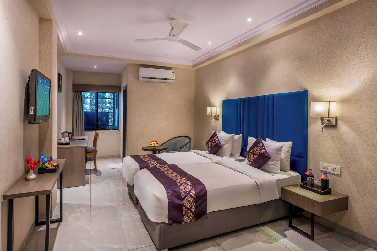 A hotel room with a large bed, a desk, a chair, a TV, and an air conditioning unit.
