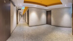 Un pasillo de hotel con piso de granito pulido, puertas de madera y un detalle amarillo en el techo.