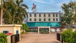 Un hotel con fachada moderna, entrada central y zona ajardinada alrededor.