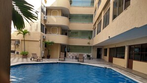 Un área de piscina con sillones reclinables y plantas en macetas.