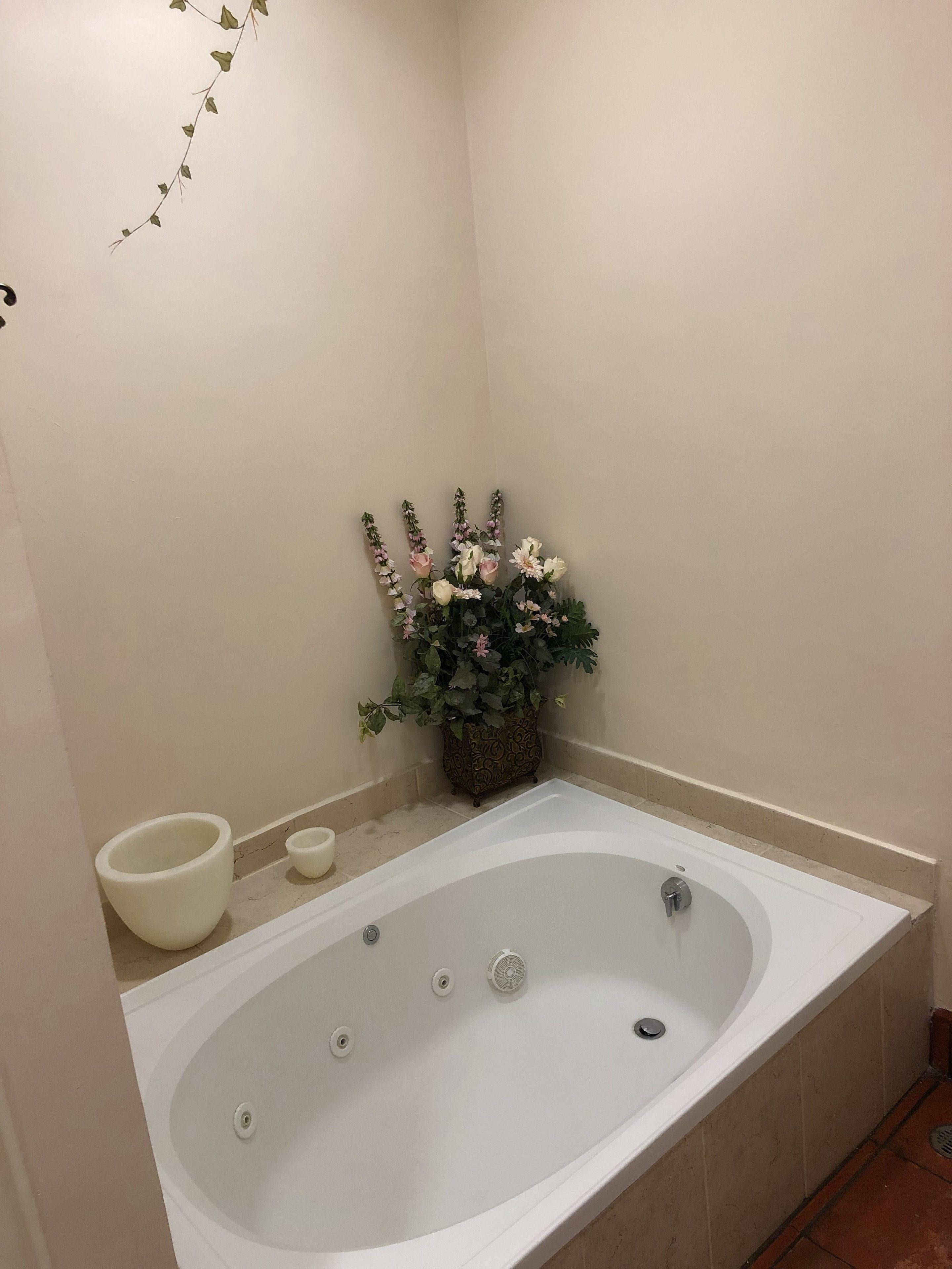 A bathroom with a bathtub, a small white basin, and a decorative plant with flowers.