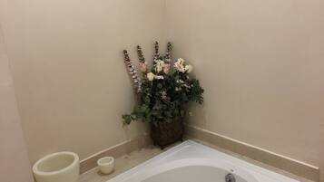 A bathroom with a bathtub, a small white basin, and a decorative plant with flowers.