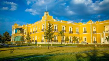 Um edifício grande e amarelo com várias varandas e uma entrada central em arco.