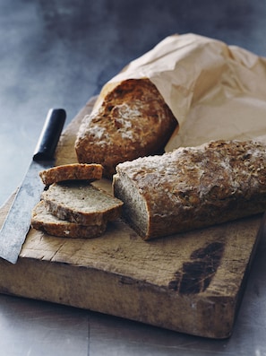 A loaf of bread on a wooden cutting board with a knife beside it.