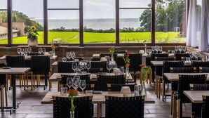 A restaurant with tables set for dining, large windows with a view of the sea and green fields, and hanging wooden light fixtures. - Comwell Klarskovgaard (Korsor)