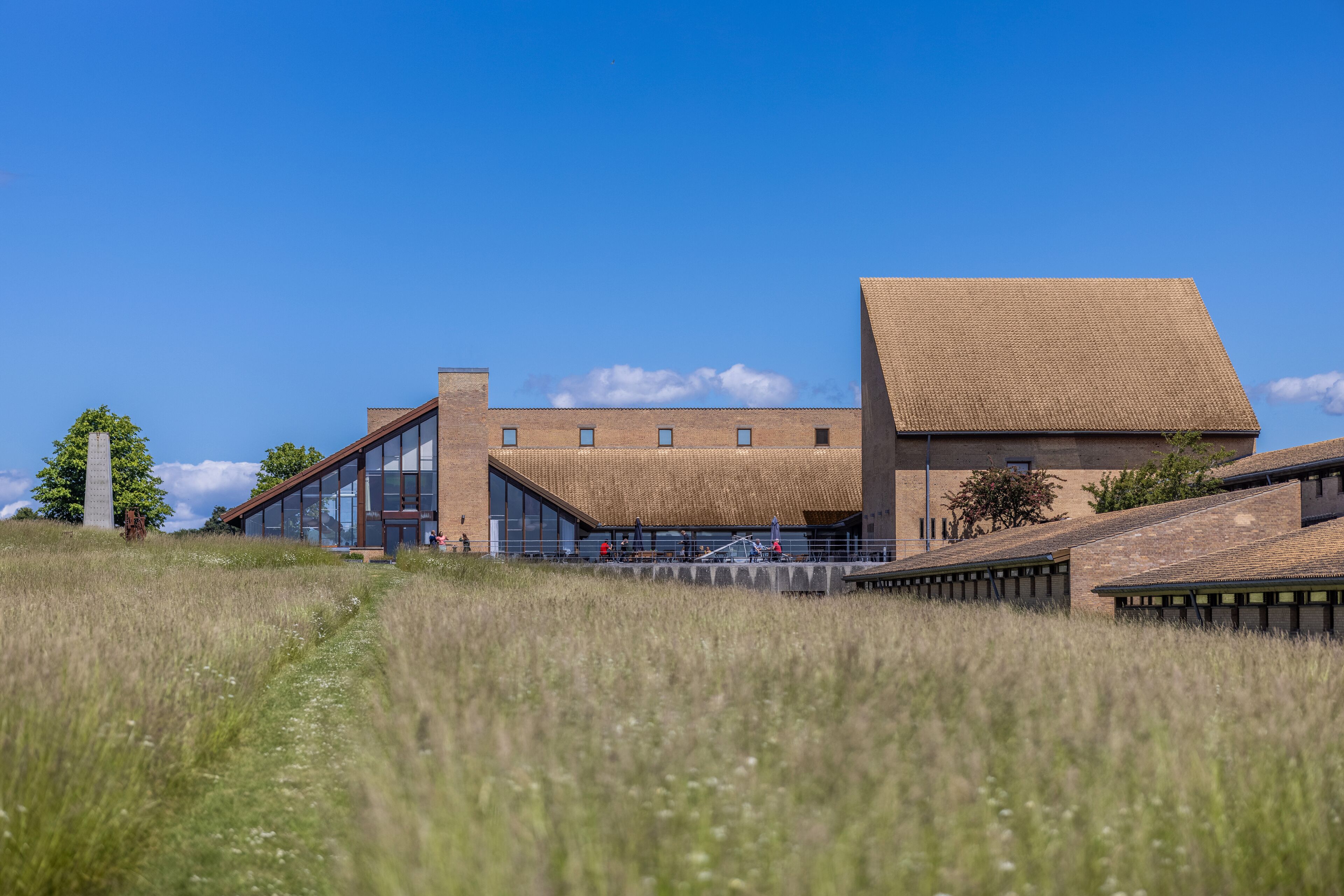 A modern building with a flat roof and large windows, situated on a grassy hill.
