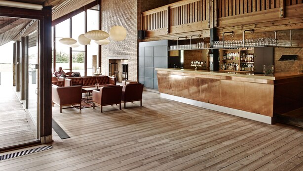 A spacious bar area with a wooden counter, seating, and a brick wall backdrop. - Comwell Klarskovgaard (Korsor)