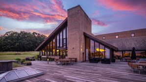 A modern building with large windows and a wooden deck with outdoor seating. - Comwell Klarskovgaard (Korsor)