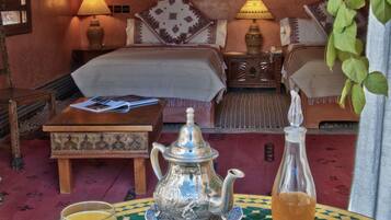 A traditional Moroccan room with a sofa, a wooden coffee table, a metal teapot, a glass of orange juice, and a bottle of tea.