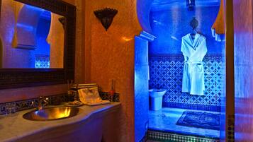 A bathroom with a sink, mirror, and a blue-lit archway leading to a shower area.