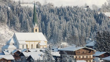 A snow-covered village with a prominent church, traditional wooden houses, and a forested mountain backdrop.