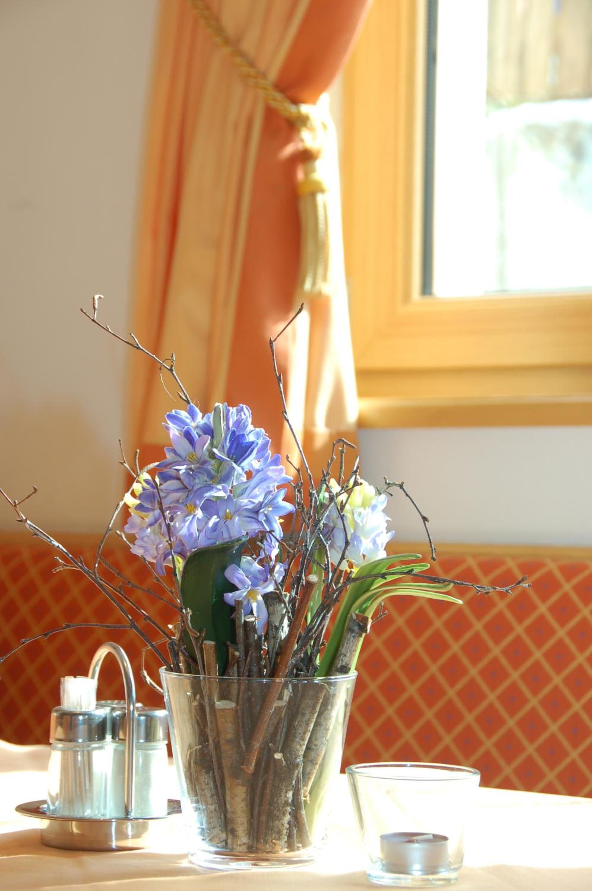 Eine transparente Glasvase mit Blumen und Zweigen auf einem Tisch.