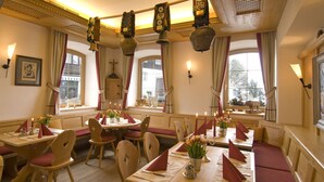 Un espace repas avec des tables et des bancs en bois, des bougies et une vue sur l’extérieur grâce à de grandes fenêtres.