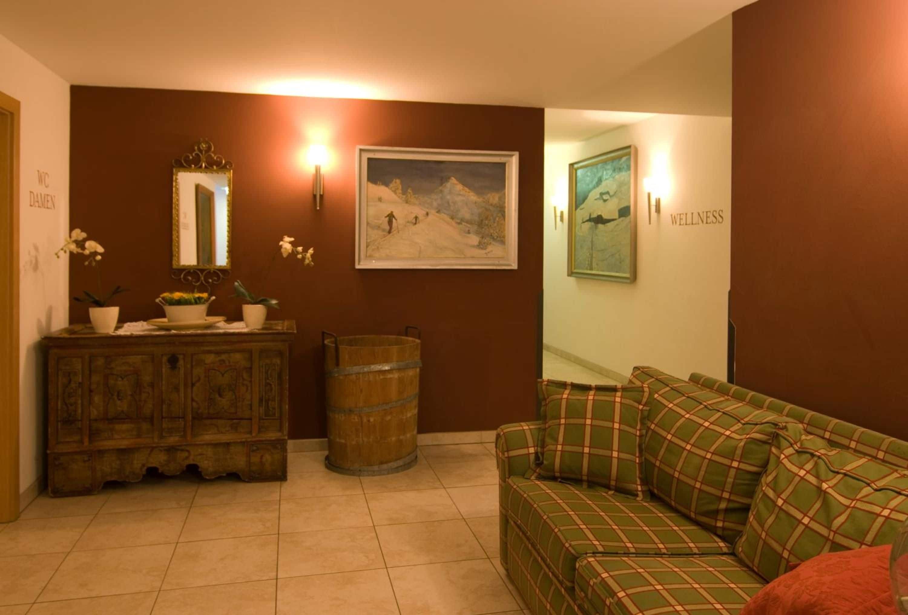 Una habitación con un armario de madera, un sofá verde a cuadros, un cuadro con un paisaje de montaña y un cartel que dice 'WELLNESS'.